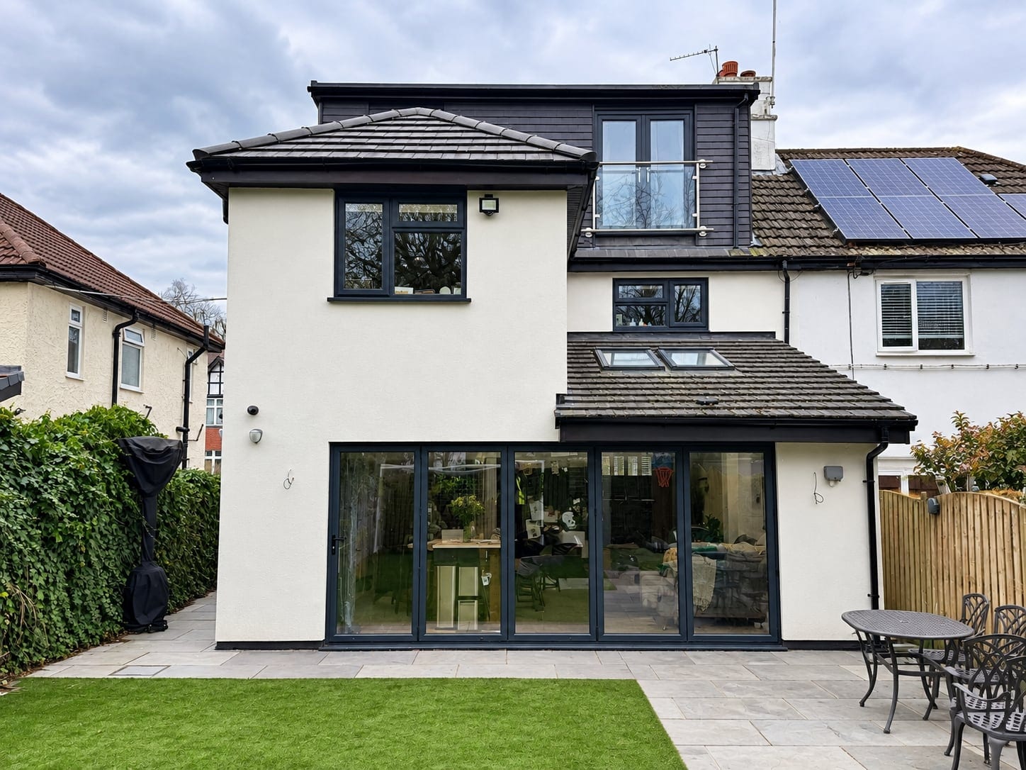 Rear of the white-rendered semi-detached house: two-storey extension, dormer and wide glazed doors