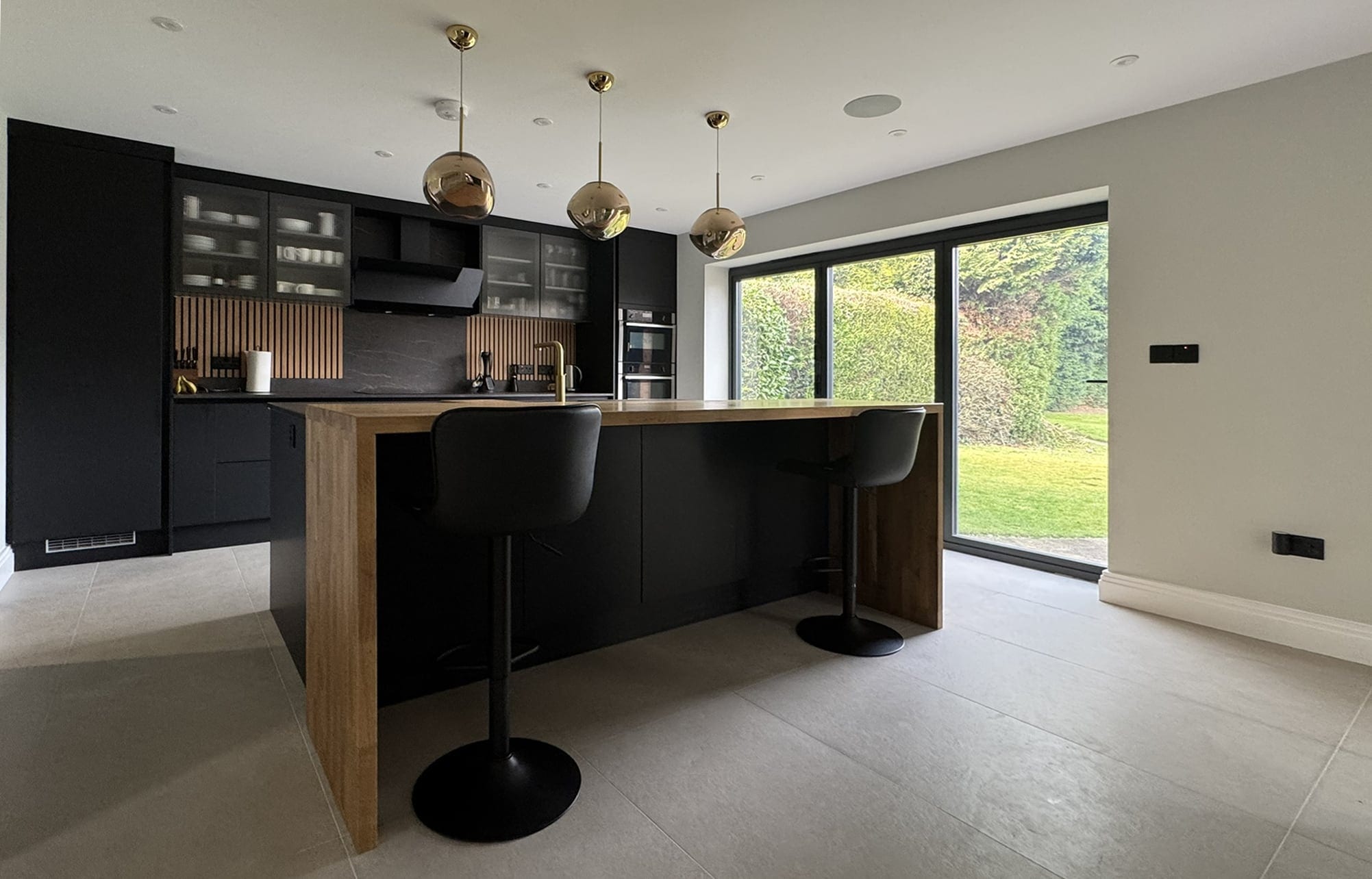 Kitchen with dark units, a timber-topped island and glazing to the garden
