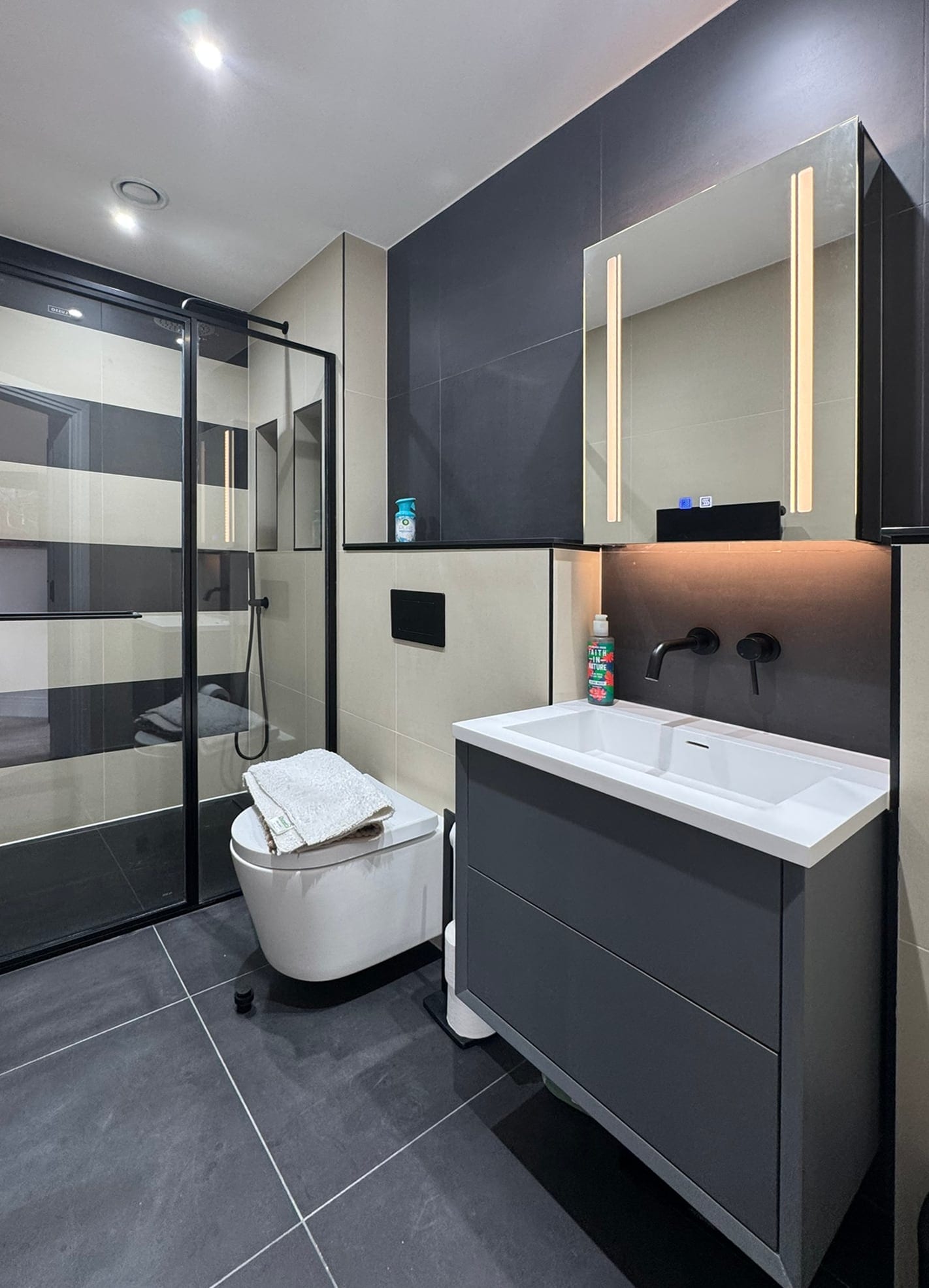 Bathroom with dark tiles and an illuminated mirror