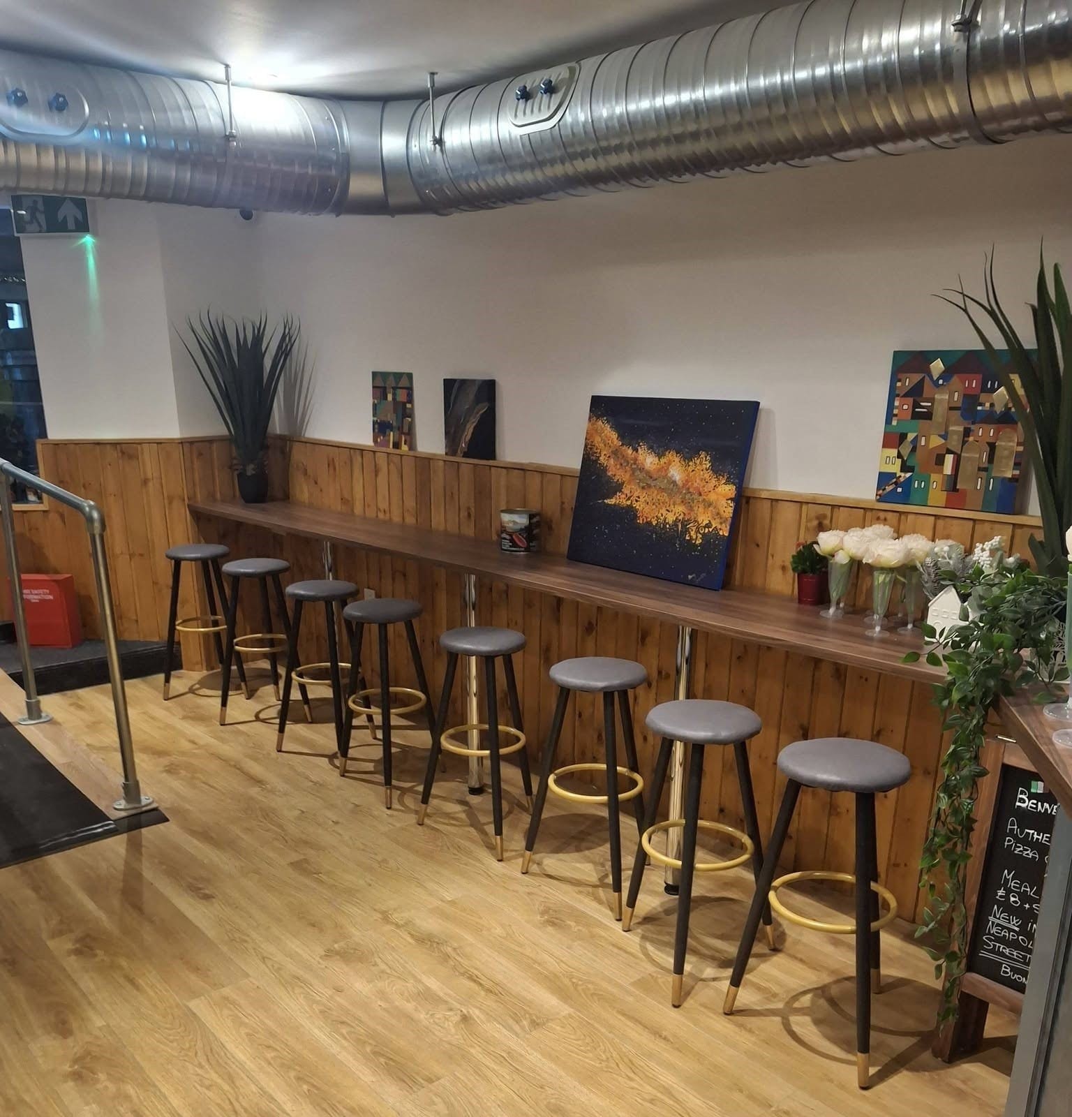 Restaurant interior with a timber-panelled wall, bar stools and exposed ducting