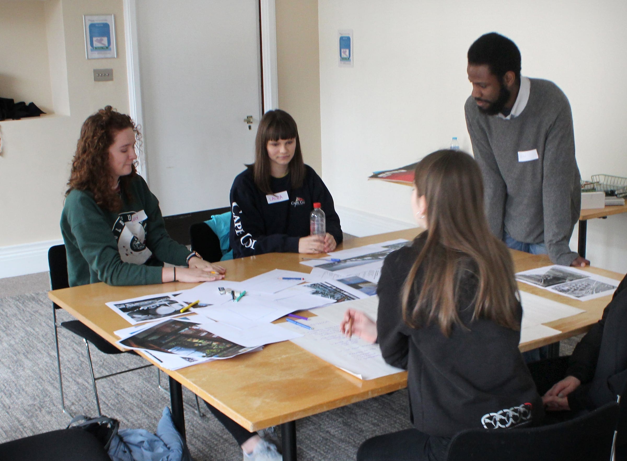 Young people working through drawings and photographs at a workshop table, with a mentor looking on