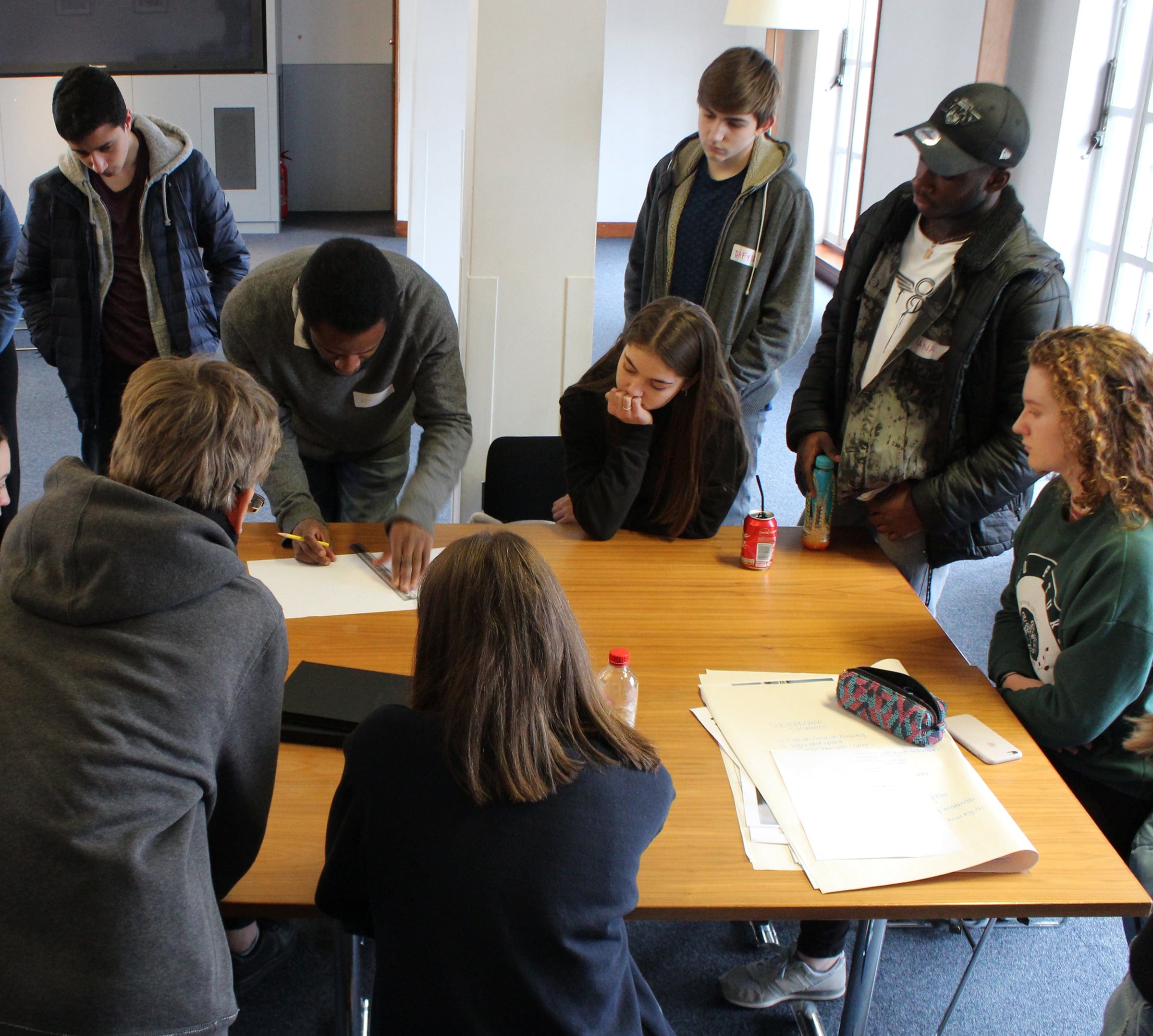 A mentor leaning over a table to sketch with a group of young participants