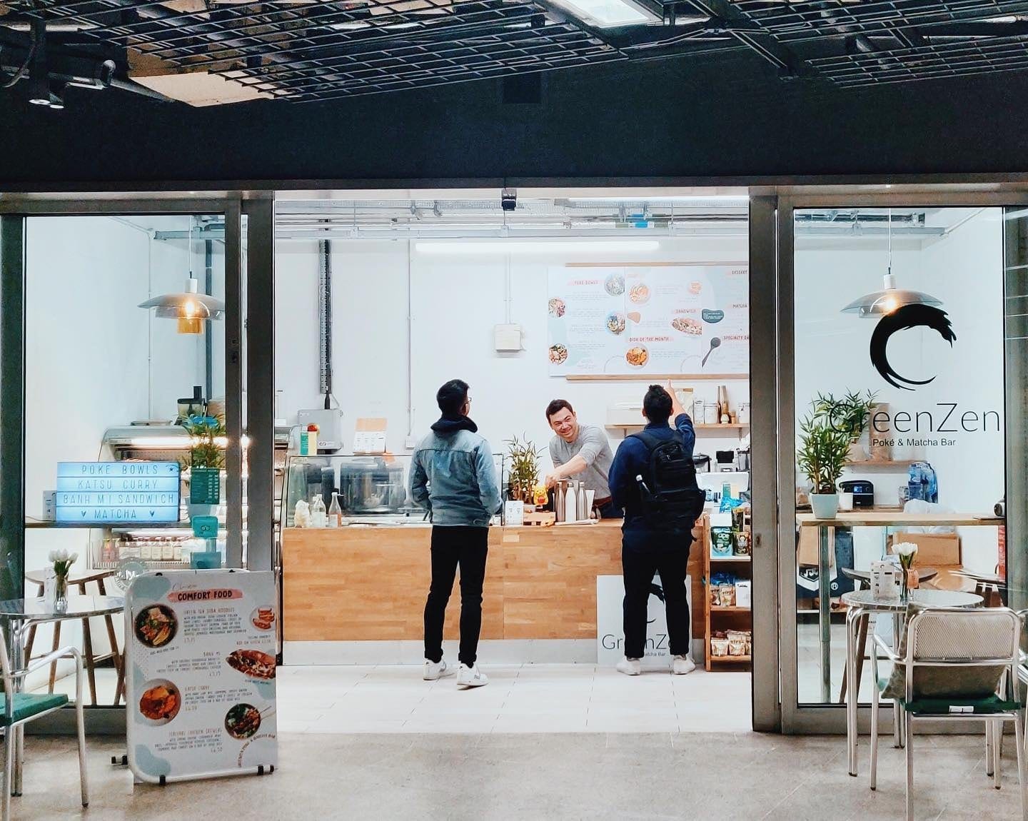 Glazed shopfront of the poké and matcha bar inside the station, with customers at the oak counter
